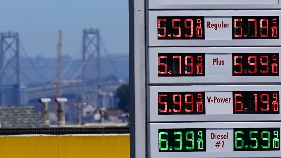 The San Francisco-Oakland Bay Bridge rises behind a gas station price board